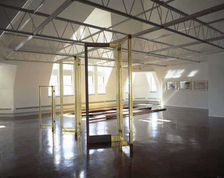 Light yellow structures resembling privacy screen frames stand in front of paddle-like wooden sculptures on the floor. 