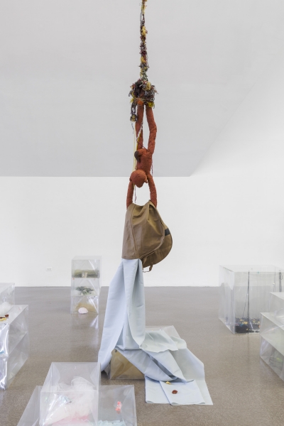 Siena rubber figure, legs dangling from a line of yarn suspended at the ceiling, holds cloth in its arms