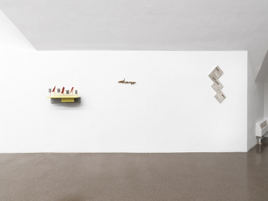 Three small sculptures on a wall, each featuring yellow or silver