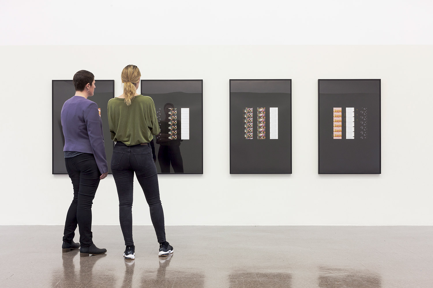 Visitors stand in front of four prints, each with three columns on a black background.
