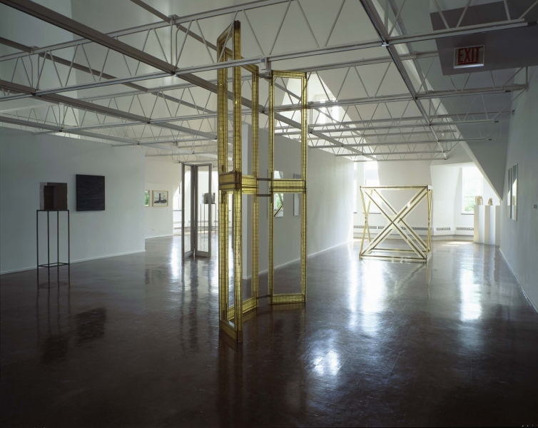 Light yellow structures resembling privacy screen frames stand in front of paddle-like wooden sculptures on the floor. 