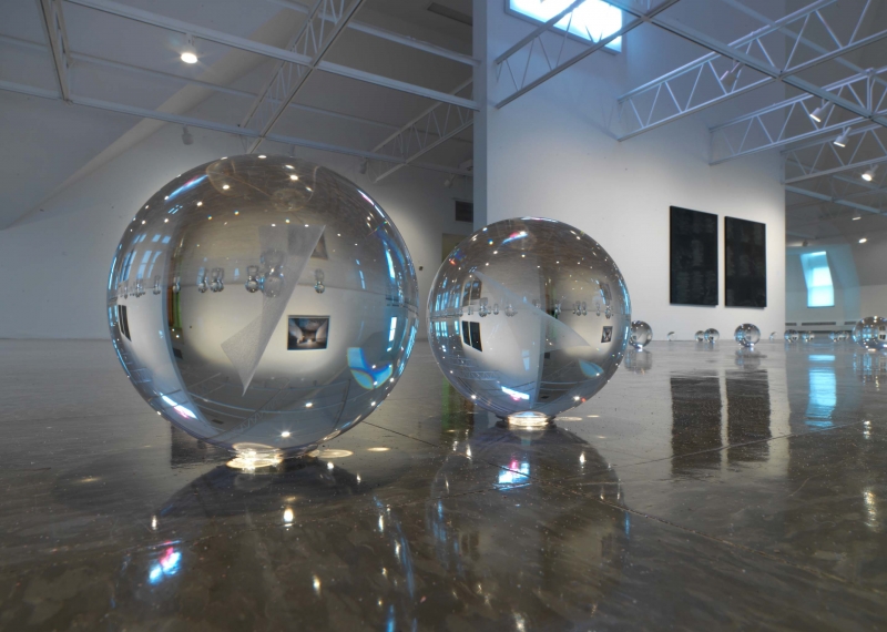 A close-up of small crystal balls on the floor, works hanging around the gallery