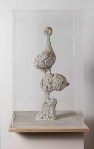 An unpainted clay sculpture, like a skinny tree with a bottom hump, two brains for branches and a pom-pom party hat on top