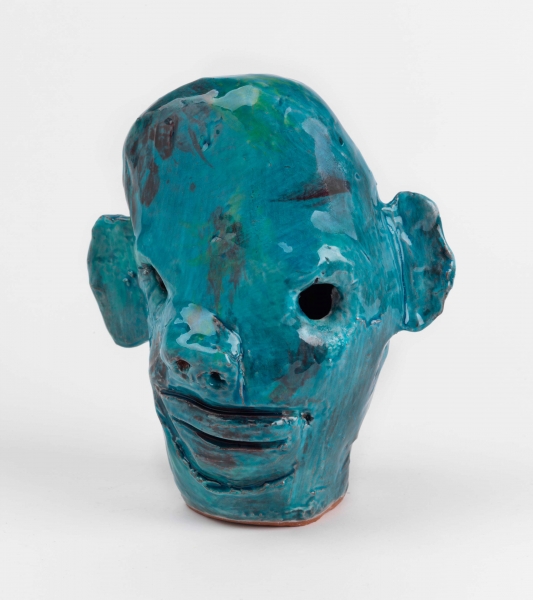 A small blue ceramic sculpture of a head, eyes poked out, tiny holes for nostrils, with splotches of deep red and green paint