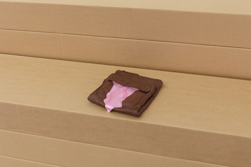 Pink slime oozes out of a brown object resembling a wallet placed on top of cardboard boxes.