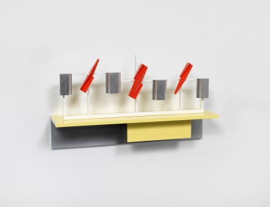 A stand of yellow cherrywood mounted on a wall with a small white, red and aluminum sculpture on top of it