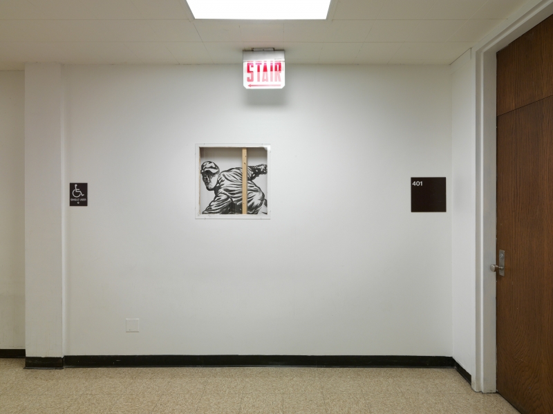 A white wall covers all but one small section of a mural, black-and-white, viewable through a square