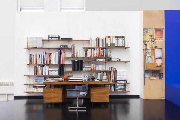 A miniature sculpture of an office desk, with swivel chair, books, hanging works and miscellaneous materials