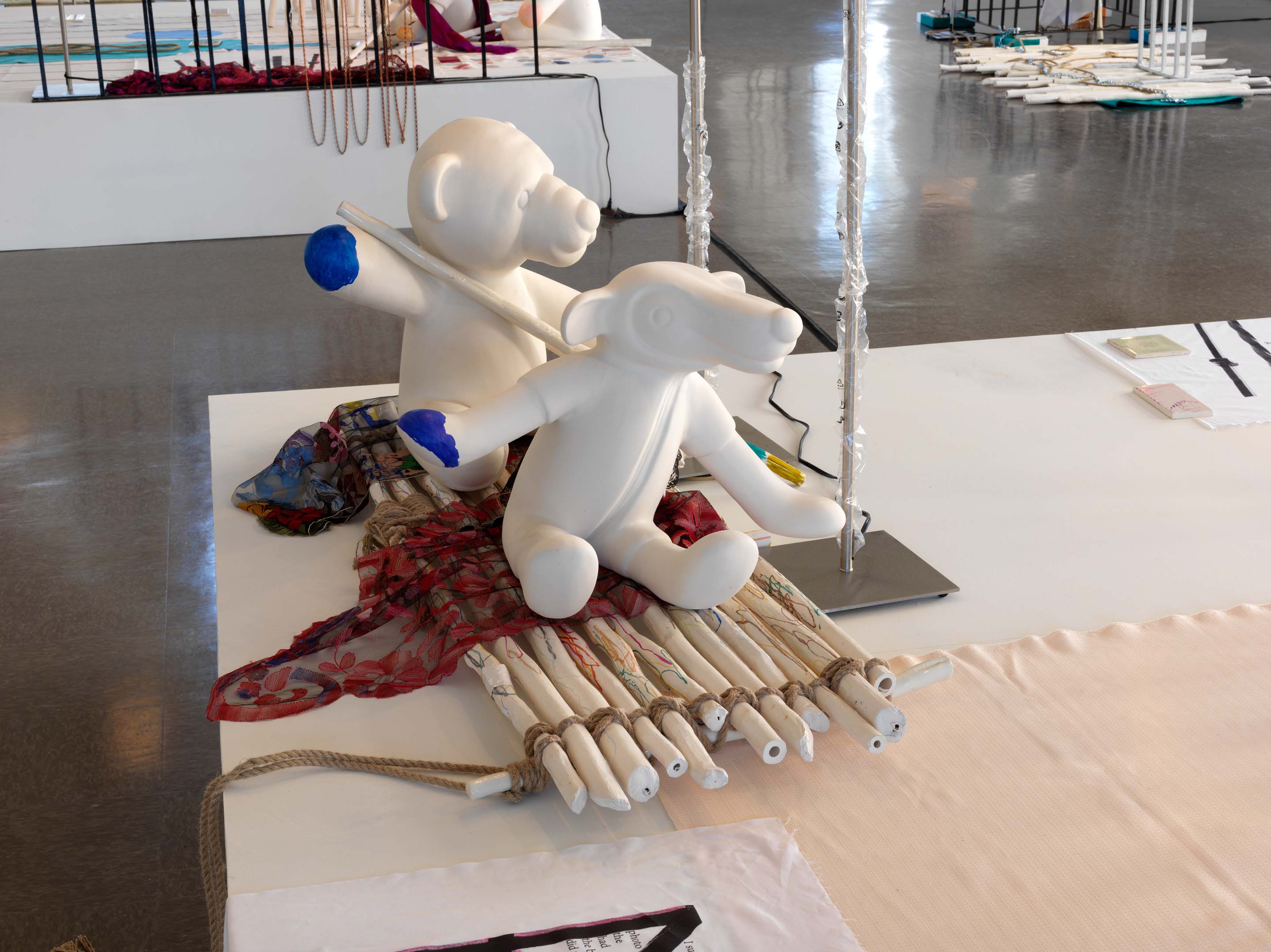 Two playful white sculptures of bears with blue paws sit on rugs covering a reed flute tied with string